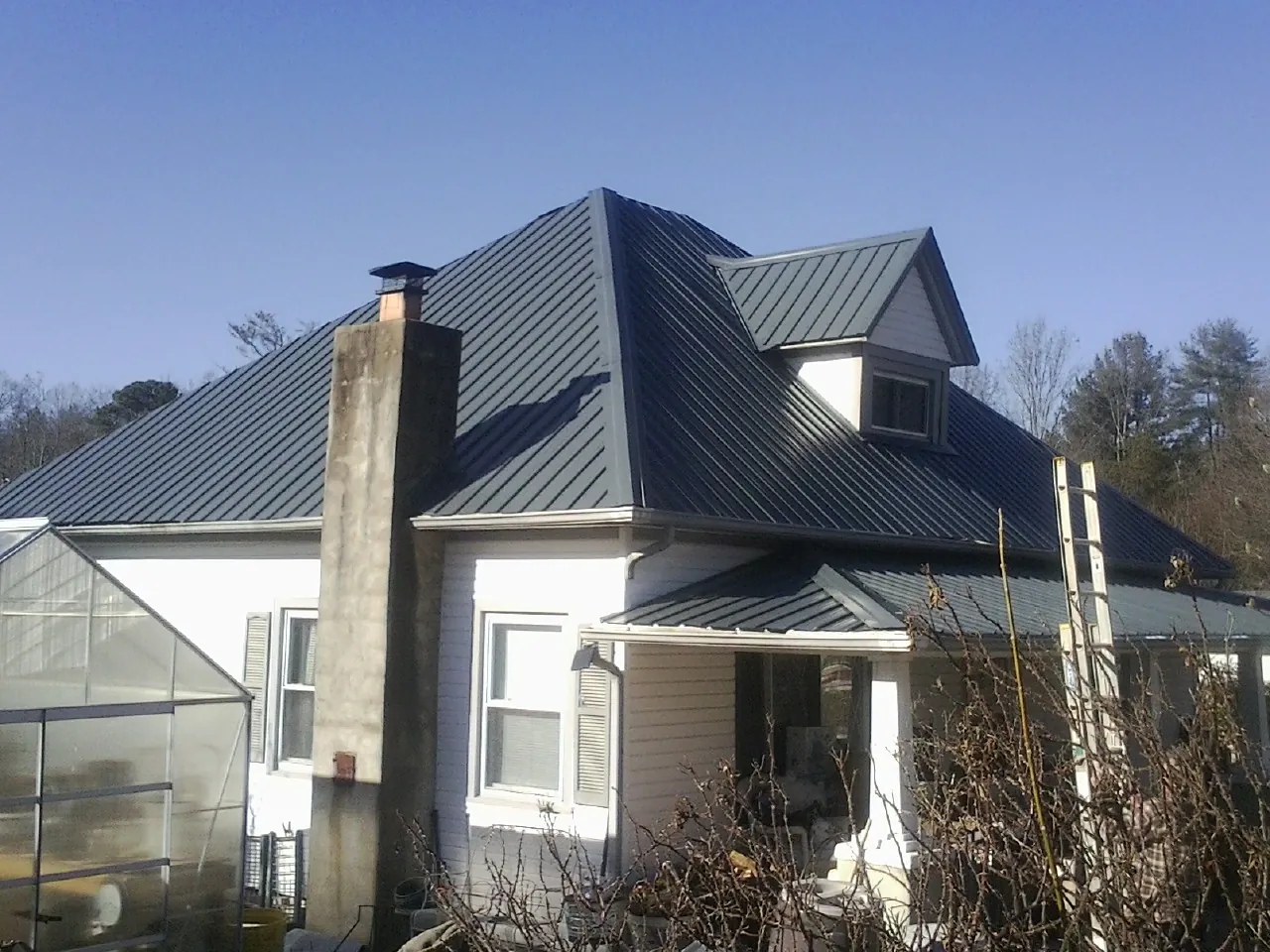 Dark blue standing seam metal roof on a white farmhouse with dormer — Slate & Tile Roof Repair by Roofing Brothers in Wesley