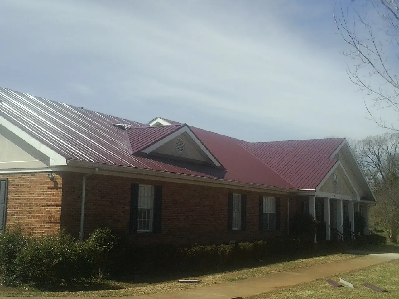 Red metal roof with gabled entries on a long brick building, from a Hail Damage Roof Repair job in Wesley