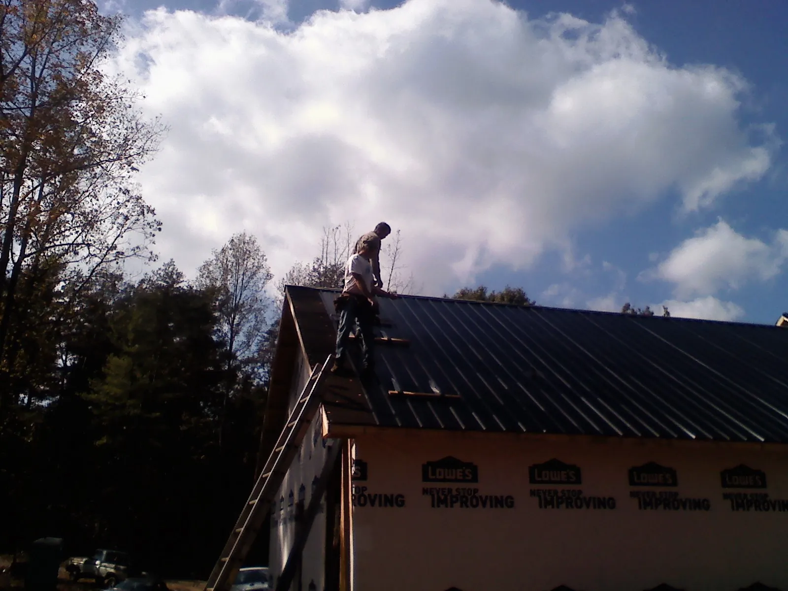 Roofer fastening dark metal panels high against a cloudy sky, from a Roof Inspection job in Wesley
