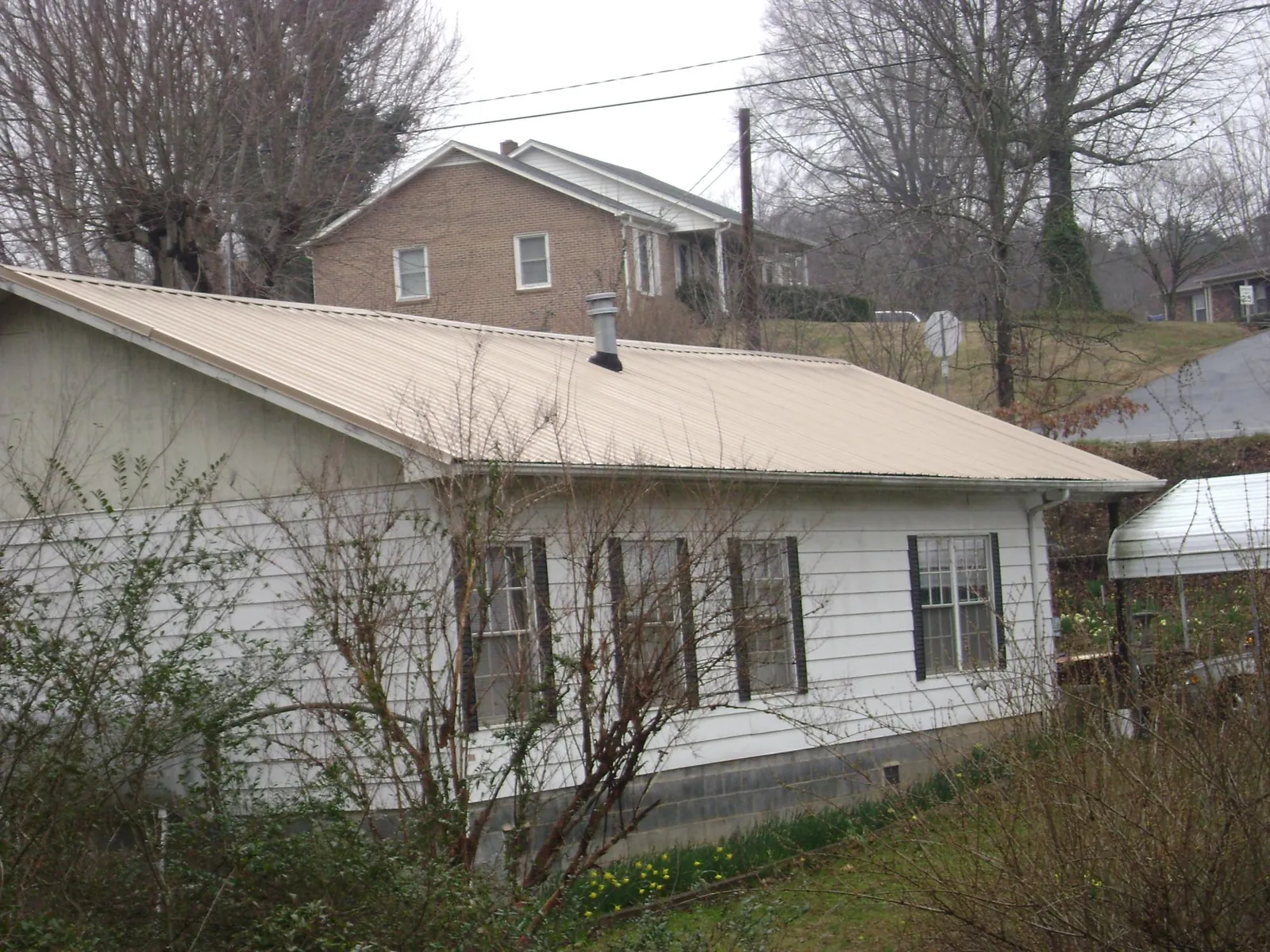 Tan metal roof on a white sided house set into a hillside — Commercial Roofing by Roofing Brothers in Wesley