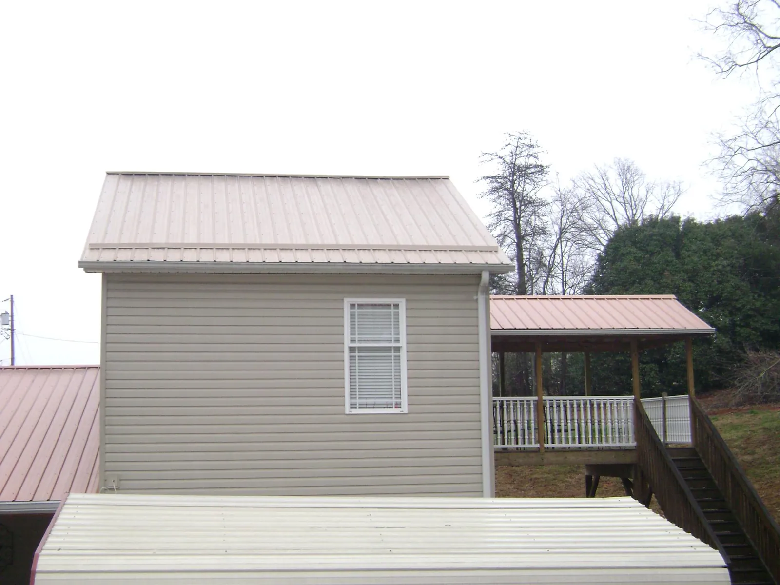 Tan metal roofs on a two story addition and attached porch, from a Roof Replacement job in Wesley